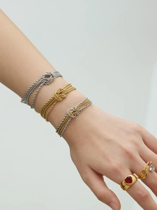 Dettaglio di tre bracciali a nodo intrecciato in oro, argento e bicolore indossati