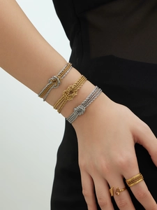 Dettaglio di bracciali a catena con nodo placcati oro 18k e anelli vintage sul polso