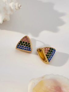 Dettaglio di orecchini a triangolo dorati con strass colorati su sfondo con conchiglia