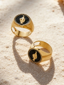 Détail de bagues en acier plaqué or 18k avec Vierge Marie sur fond de sable
