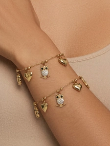 Detail eines 18k vergoldeten Eulen- und Herzanhänger-Armbands mit Zirkonia am Handgelenk