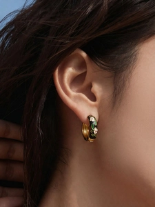 Detail of floral enamel hoop earring with white flowers and green leaves on a model