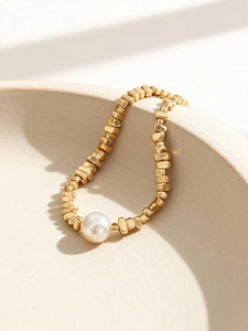 Detail eines Armbands mit unregelmäßigen Goldwürfeln und weißer Perle auf Keramik