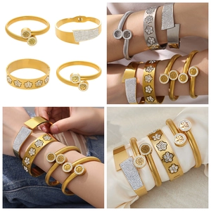Dettaglio di bracciali in acciaio dorato con motivi a fiori, albero della vita e zirconi