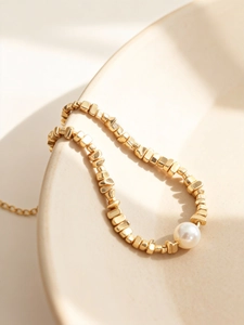 Detailaufnahme von unregelmäßigen Goldperlen und einer weißen Perle an einer Kette