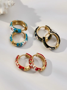 Detail of three colorful enamel floral hoop earrings in blue black and red on a shell