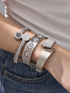 Dettaglio di bracciali sovrapposti in acciaio inox argento con albero della vita e fiori