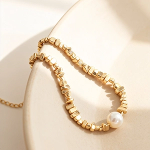 Goldenes Perlenarmband mit unregelmäßigen Perlen und weißer Perle auf Keramikteller