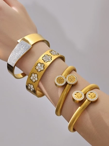Dettaglio di quattro bracciali in acciaio dorato con zirconi e ciondoli a forma di fiore