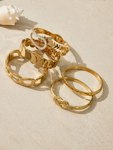 Nahaufnahme goldener geometrischer Armbänder mit Zirkon auf beigem Steinboden