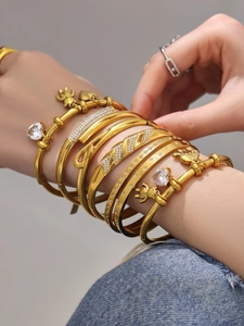 Close-up of layered 18k gold plated stainless steel bangles with heart zircon and bear charm