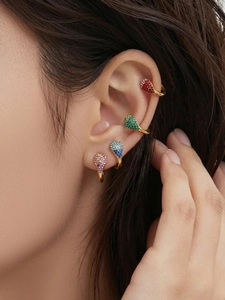 Gros plan de boucles d'oreilles goutte d'or serties de zircons colorés sur l'oreille