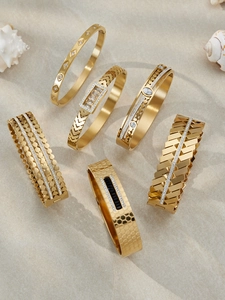 Detailed close-up of 18k gold-plated geometric bangles with zircon inlay on sand