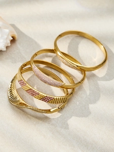 Detailed view of four 18k gold plated stainless steel bangles with zircons on sand