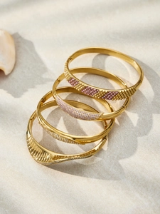 Macro detail of four gold-plated bangles with zircons on a textured sandy base