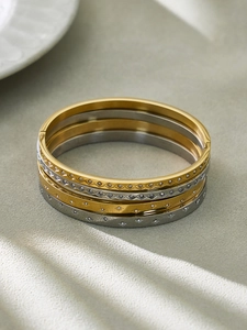 Close-up of 18k gold and silver stackable bangles with geometric star patterns and cubic zirconia