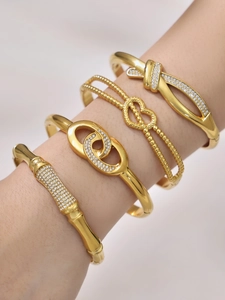 Close-up of four gold bracelets featuring zircon bow and interlocking heart designs