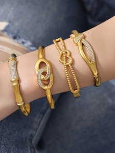 Close-up of four gold bracelets with zircon heart and bow details on a wrist