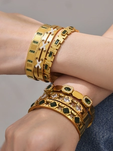 Close-up of stacked gold bangles featuring emerald green stones and diamond patterns