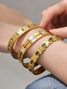 Detail of 18k gold plated bracelets featuring green gems and hollow diamond-set X patterns