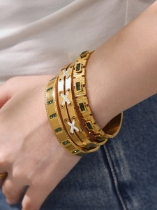 Close-up of stacked 18k gold plated bangles with emerald stones and micro-pave diamonds