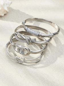 Close-up of four silver stainless steel bracelets with cubic zirconia on a stone surface