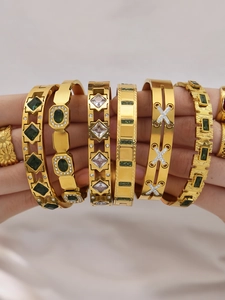 Detail of 18k gold-plated bangles set with emerald gemstones and sparkling crystals