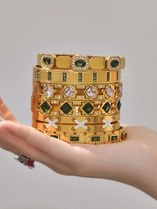 Close-up of six gold-plated bangles with emerald green and white cubic zirconia crystals