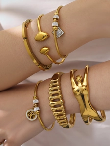 Dettaglio di bracciali placcati oro sovrapposti con ciondolo albero della vita e zirconi