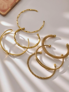 Detail van gouden armbanden in bamboestijl en spiraalontwerp met elegante bladschaduwen