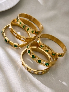 Close-up of gold geometric bangles with green and white cubic zirconia accents