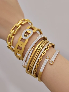 Detalle de brazaletes apilados en acero chapado en oro 18k con circonitas brillantes