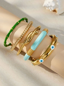 Dettaglio di cinque bracciali dorati sovrapposti con malocchio e trame di bambù