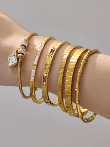 Detalle de brazaletes de acero chapado en oro de 18k con circonitas y números romanos