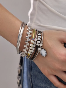 Detailansicht silberner Armbänder mit glitzernden Strasssteinen und weißem Steinanhänger