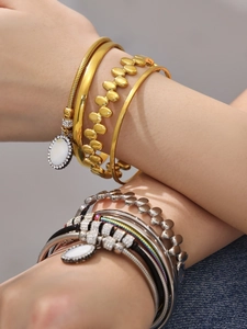 Nahaufnahme geschichteter Gold- und Silberarmbänder mit Strassbesatz am Handgelenk