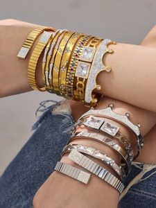 Nahaufnahme gestapelter Gold- und Silberarmbänder mit Zirkonia und Kronendesign vor Denim