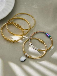 Detail von fünfteiligem Edelstahlschmuck-Set mit goldenen Armreifen und Schlangenarmbändern