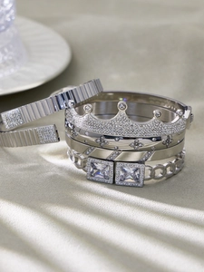 Detailaufnahme von silbernen Kronen- und Zirkon-Armbändern auf strukturiertem Grund