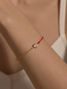 Dettaglio di un bracciale con cordino rosso e catena dorata con zircone rosa intarsiato