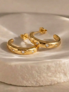 Nahaufnahme goldener C-Ohrringe mit Zirkonia-Sternen auf einem weißen Teller