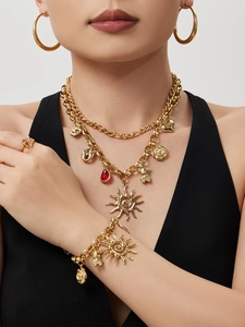 Detail of a chunky gold jewelry set with sun, bear, and red gemstone charms on a model
