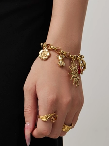 Detailed close-up of golden charm bracelet with teddy bear, sun, and gemstone pendants