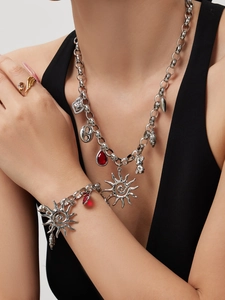 Detail of chunky link chain necklace and bracelet with sun, heart, and red drop pendants