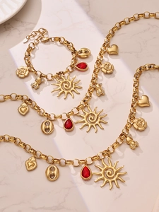 Detail of gold-plated necklaces with red zircon teardrops and heart charms on marble
