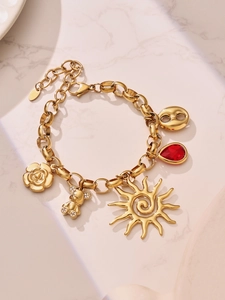 Detail of a gold stainless steel bracelet featuring bear, sun, and ruby pendants