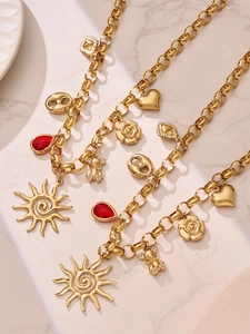 Detail of gold-tone chunky link necklace with sun, bear, and red drop charms on marble