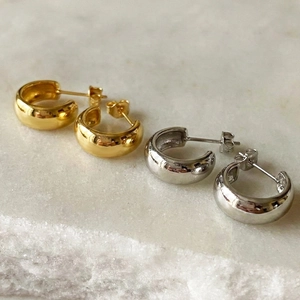 Minimalistische klobige C-förmige Creolen in Gold und Silber auf Marmorhintergrund