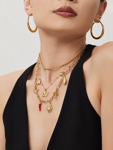 Detail of layered gold-plated necklaces with cross and red chili charm on a model