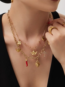 Detail of layered gold necklaces with charms like angel, clover, and heart on a black outfit
